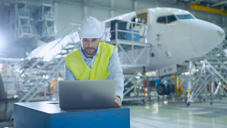 Engineer Working On A Test Environment On A Laptop With A Plane In The Background