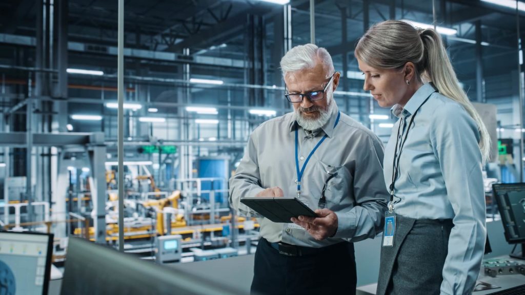 Male and Female Executives Looking at a Tablet in a Factory