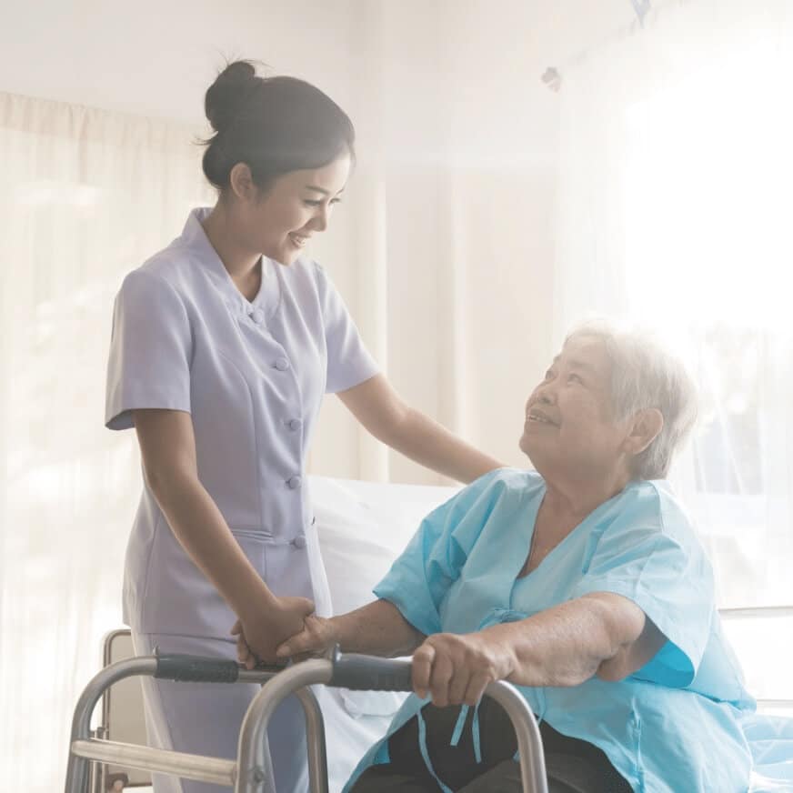 Female Nurse Assisting an Older Woman Get Out of Bed