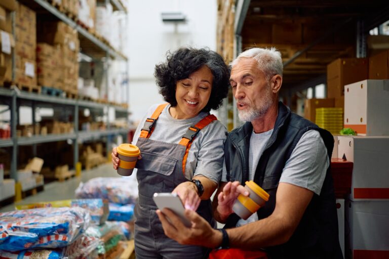 Happy,warehouse,worker,and,her,colleague,using,smart,phone,while, communication in the workplace