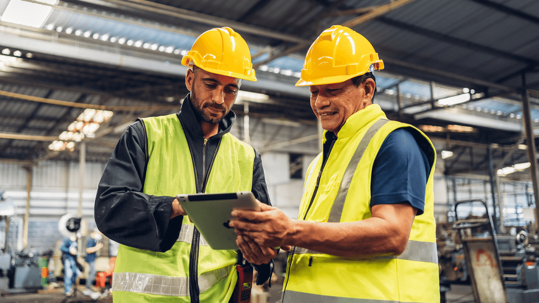 Two Workers In Protective Equipment Look Over A Tablet With Shift Scheduling Software.