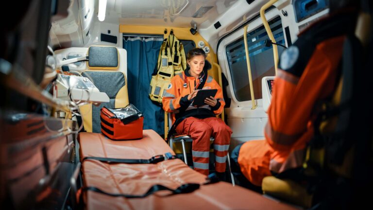 A female EMS worker checking a scheduling app while riding in the back of an ambulance.