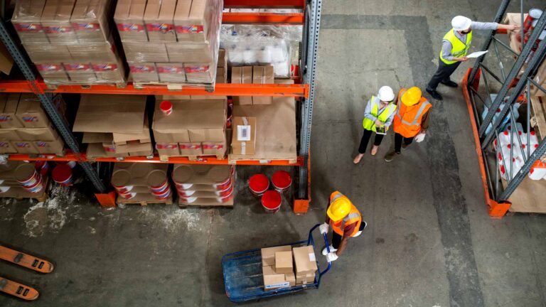 Overhead view photograph of four workers in a warehouse wearing safety vests.
