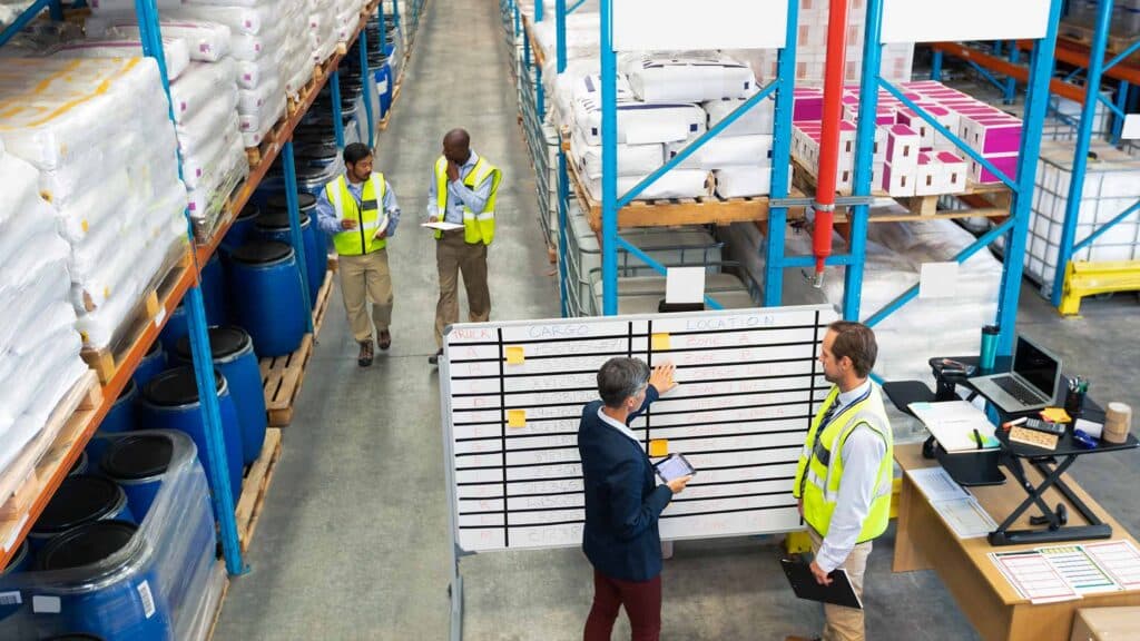 A stock photo of a supervisor viewing a complex, multi-shift industrial schedule with his team in a plant setting.