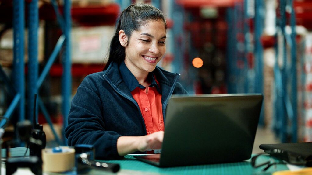 A person using workforce management software on a laptop to schedule shifts in a warehouse setting.